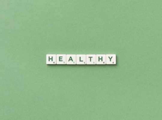 Scrabble tiles spelling the word 'healthy' on a light green background, top view.