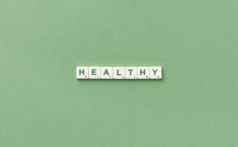Scrabble tiles spelling the word 'healthy' on a light green background, top view.