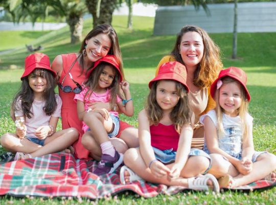 Friends enjoying a sunny day picnic on grass with bucket hats and smiles in a Portuguese park.