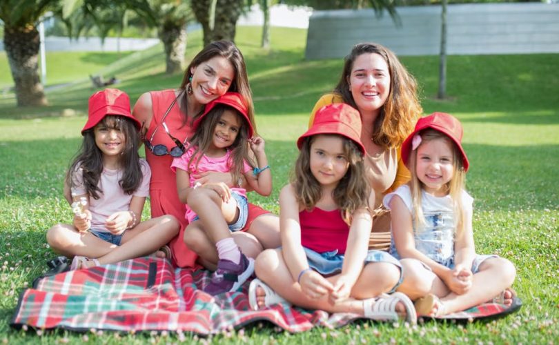 Friends enjoying a sunny day picnic on grass with bucket hats and smiles in a Portuguese park.